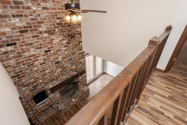 stairs featuring ceiling fan, wood-type flooring, and a brick fireplace