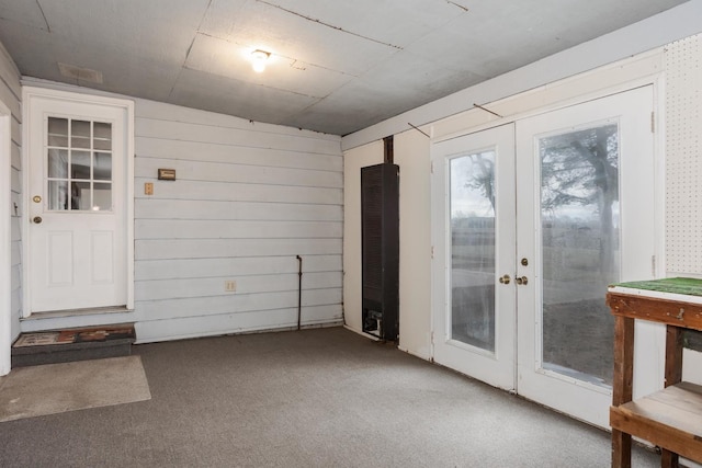 doorway with carpet flooring, wood walls, and french doors