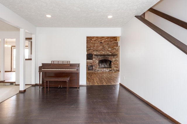 unfurnished living room with a textured ceiling, dark hardwood / wood-style flooring, a brick fireplace, and a notable chandelier