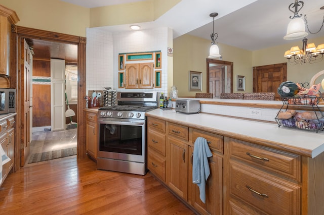 kitchen featuring hanging light fixtures, stainless steel appliances, a notable chandelier, light hardwood / wood-style floors, and tasteful backsplash