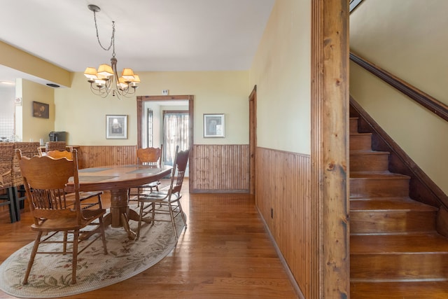 dining area with a notable chandelier, wood-type flooring, and wood walls