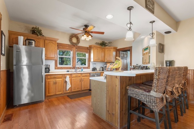 kitchen featuring ceiling fan, a kitchen breakfast bar, stainless steel refrigerator, light hardwood / wood-style flooring, and decorative light fixtures