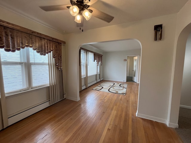 empty room with ceiling fan, plenty of natural light, a baseboard radiator, and light hardwood / wood-style floors