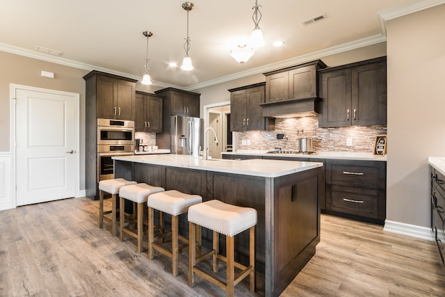 kitchen featuring appliances with stainless steel finishes, a kitchen island with sink, and light wood-type flooring