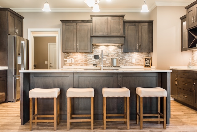 kitchen featuring crown molding, stainless steel fridge with ice dispenser, hanging light fixtures, and light wood-type flooring