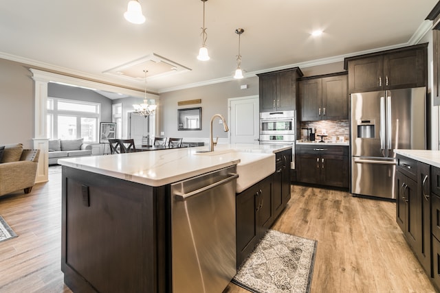 kitchen featuring an island with sink, dark brown cabinetry, stainless steel appliances, and light wood-type flooring