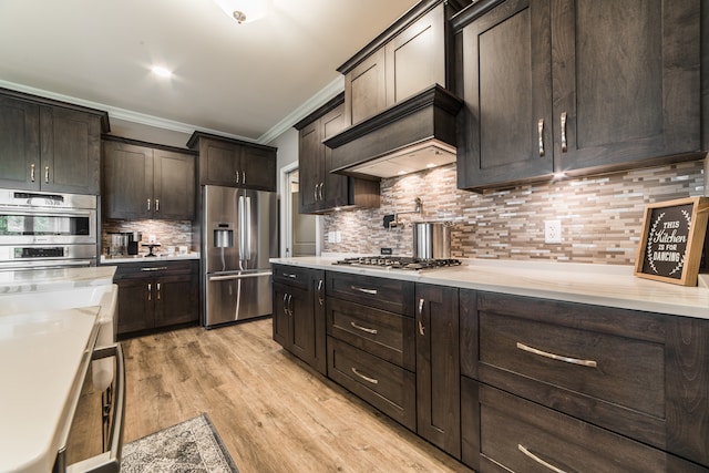 kitchen with ornamental molding, appliances with stainless steel finishes, light hardwood / wood-style floors, and tasteful backsplash