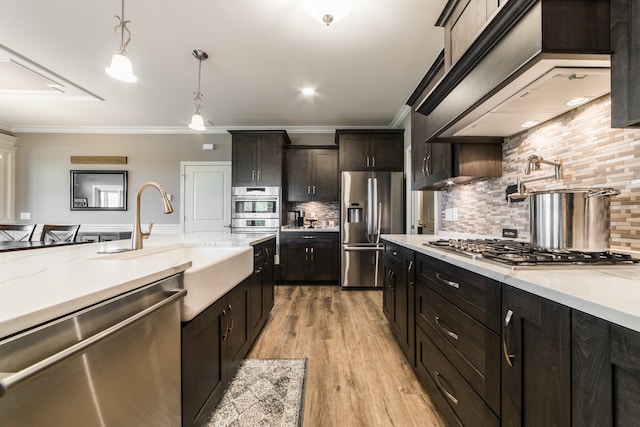 kitchen featuring decorative backsplash, stainless steel appliances, ornamental molding, pendant lighting, and light hardwood / wood-style floors