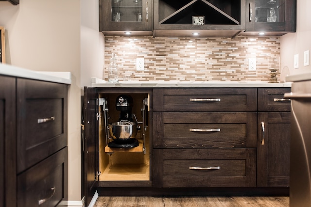 bar with backsplash, dark brown cabinets, and light wood-type flooring