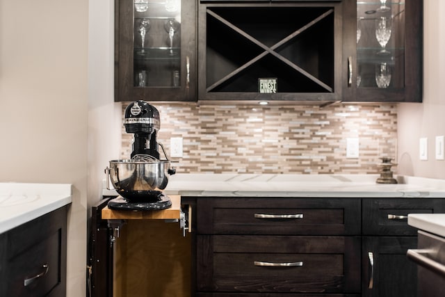 bar with light stone counters, dark brown cabinets, and backsplash