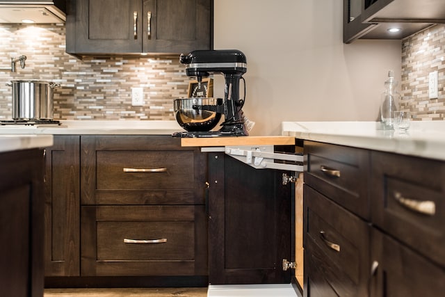 bar featuring tasteful backsplash, dark brown cabinetry, and exhaust hood