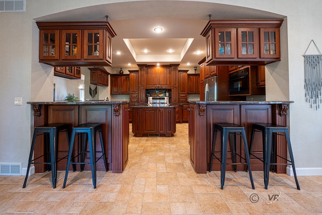 kitchen featuring stainless steel appliances, a raised ceiling, kitchen peninsula, and a kitchen breakfast bar