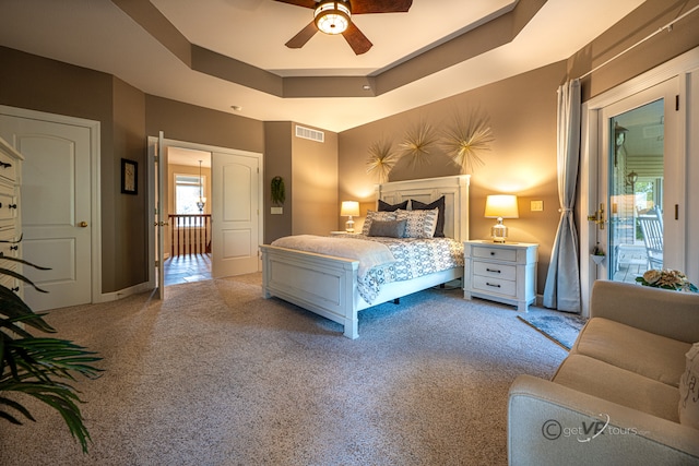 carpeted bedroom with access to exterior, ceiling fan, and a raised ceiling