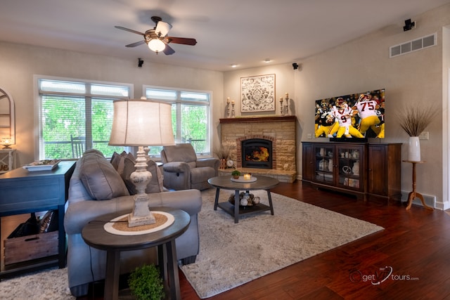 living room featuring ceiling fan, a stone fireplace, and dark hardwood / wood-style flooring