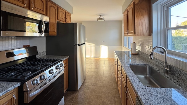 kitchen featuring backsplash, appliances with stainless steel finishes, light stone countertops, sink, and tile patterned flooring