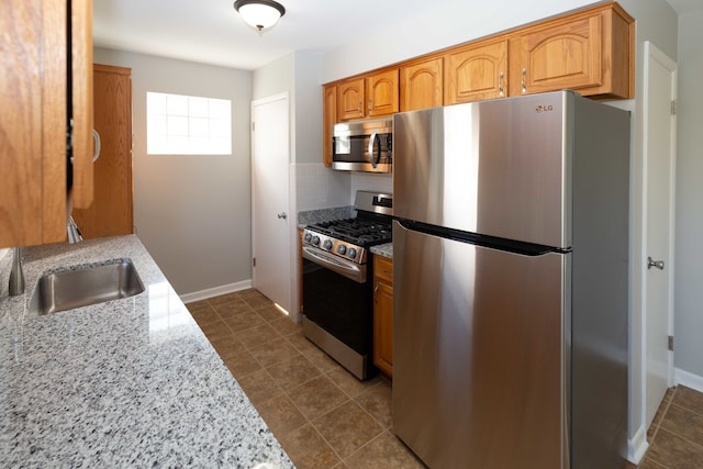 kitchen with decorative backsplash, light stone counters, appliances with stainless steel finishes, dark tile patterned flooring, and sink