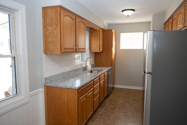 kitchen featuring dark tile patterned flooring, light stone countertops, appliances with stainless steel finishes, sink, and decorative backsplash