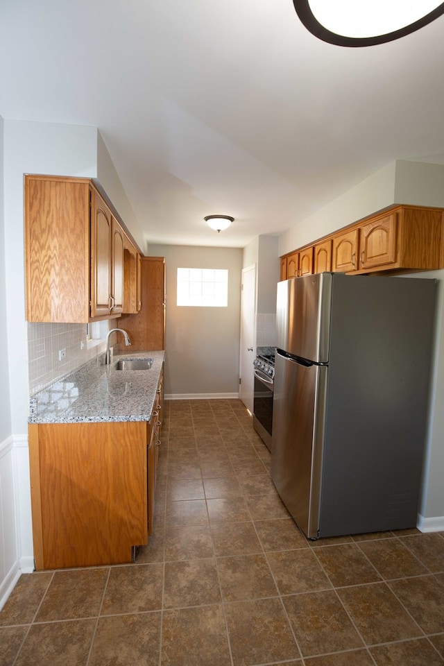 kitchen featuring dark tile patterned flooring, appliances with stainless steel finishes, sink, light stone counters, and decorative backsplash