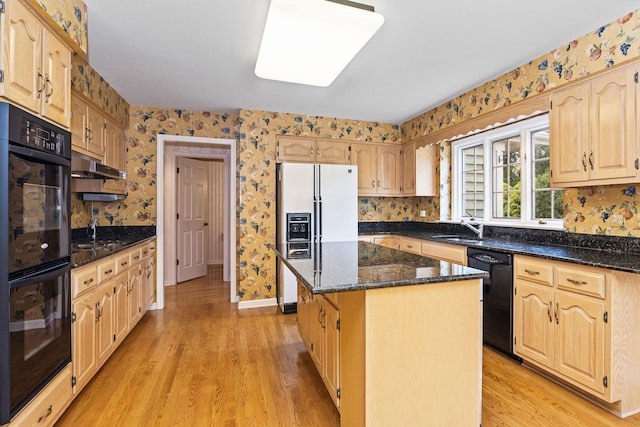 kitchen featuring light hardwood / wood-style flooring, sink, dark stone counters, black appliances, and a center island