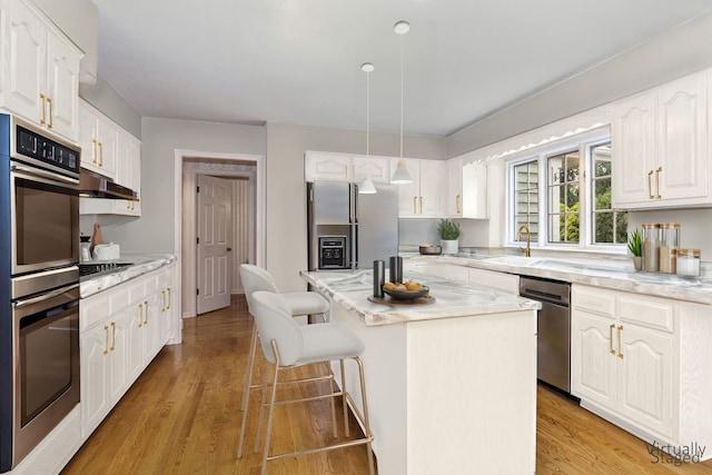 kitchen featuring light wood-type flooring, light stone counters, stainless steel appliances, white cabinets, and a kitchen island