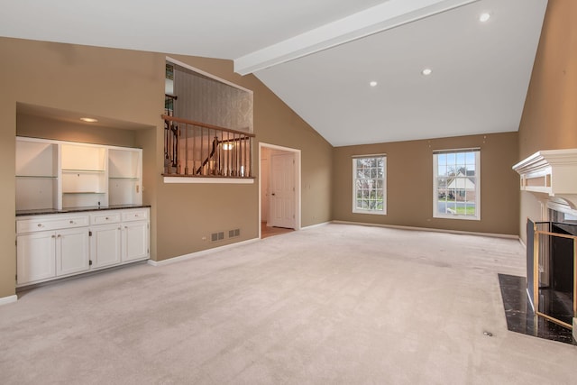 unfurnished living room featuring a fireplace, beam ceiling, high vaulted ceiling, and light colored carpet