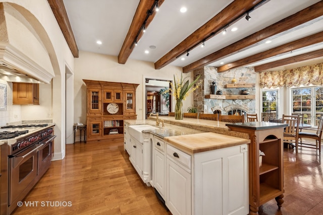 kitchen with white cabinets, high end stove, a large island with sink, beamed ceiling, and light hardwood / wood-style floors