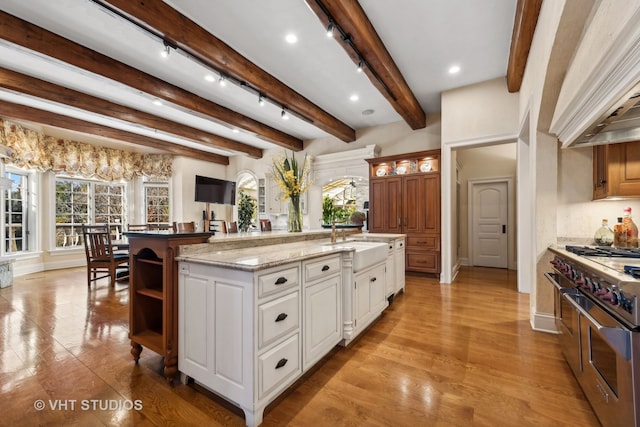 kitchen featuring white cabinetry, sink, beamed ceiling, high end stove, and a kitchen island with sink