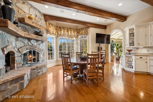 dining area with beamed ceiling, a stone fireplace, and light hardwood / wood-style flooring