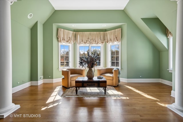 living area featuring decorative columns, wood-type flooring, and vaulted ceiling