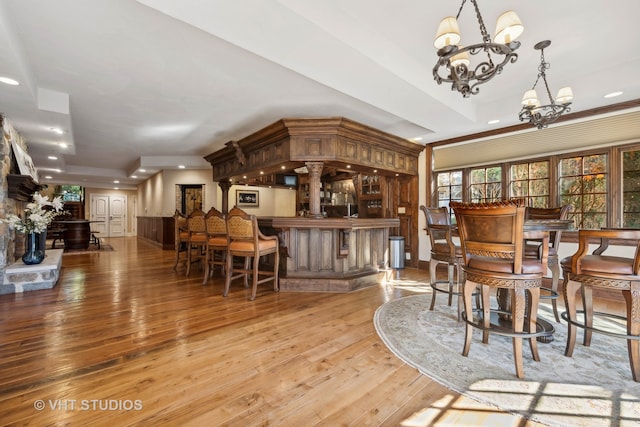 dining room with a raised ceiling, bar, light hardwood / wood-style flooring, and a chandelier