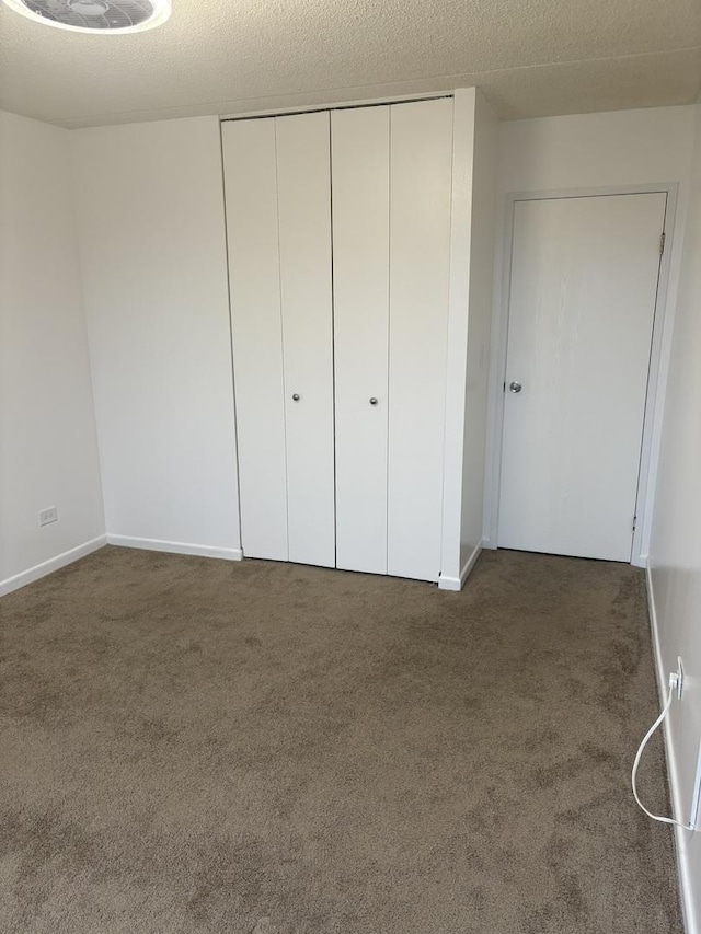 unfurnished bedroom with a textured ceiling, dark carpet, and a closet