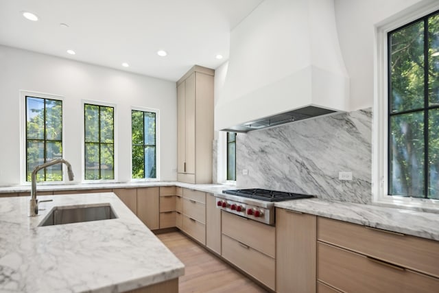 kitchen with light brown cabinetry, light stone counters, premium range hood, and sink