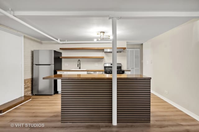 kitchen with gas stove, light wood-type flooring, sink, and stainless steel fridge