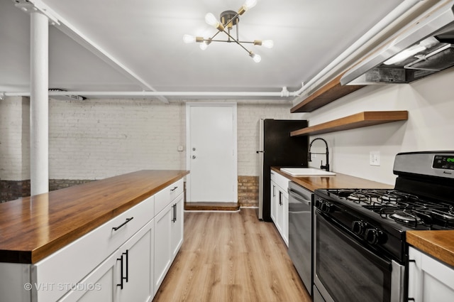 kitchen with wooden counters, light wood-type flooring, appliances with stainless steel finishes, white cabinets, and brick wall