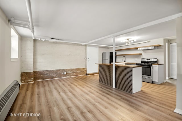 kitchen with light hardwood / wood-style flooring, a baseboard heating unit, appliances with stainless steel finishes, and brick wall