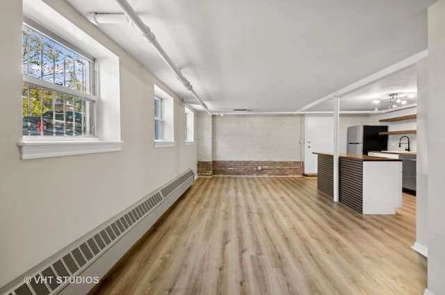 interior space with light hardwood / wood-style flooring, brick wall, sink, and a baseboard heating unit