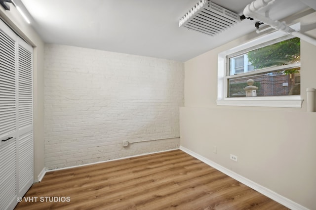 unfurnished bedroom with wood-type flooring, brick wall, and a closet