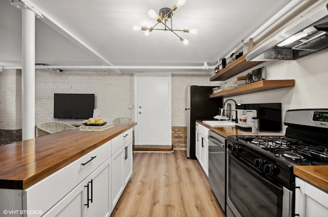 kitchen with butcher block countertops, white cabinetry, appliances with stainless steel finishes, light hardwood / wood-style floors, and brick wall