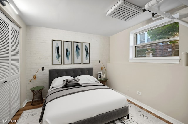 bedroom with brick wall, hardwood / wood-style flooring, and a closet