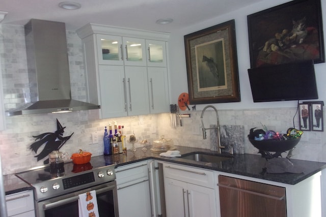 kitchen with wall chimney range hood, white cabinets, backsplash, appliances with stainless steel finishes, and sink