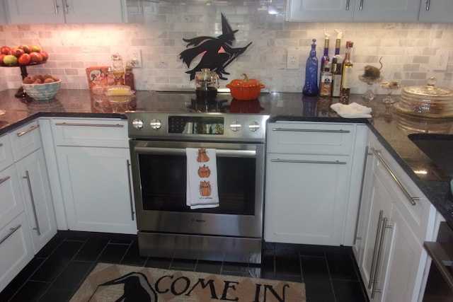 kitchen with dark tile patterned floors, backsplash, dark stone counters, electric range, and white cabinets