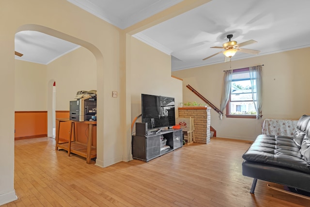 living room with light wood-type flooring, crown molding, ceiling fan, and a fireplace