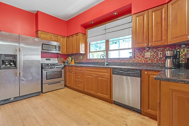 kitchen with sink, light hardwood / wood-style flooring, backsplash, appliances with stainless steel finishes, and dark stone counters