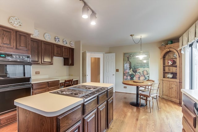 kitchen with black double oven, light hardwood / wood-style flooring, hanging light fixtures, a kitchen island, and stainless steel gas stovetop