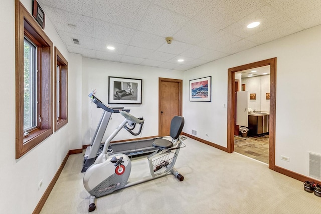 workout room with a paneled ceiling and light colored carpet