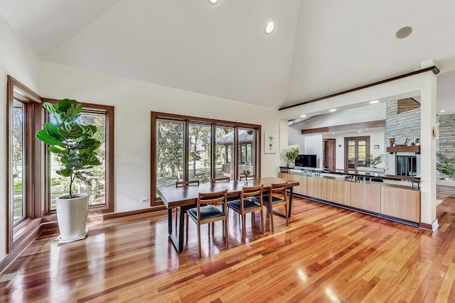 dining room with a large fireplace, plenty of natural light, high vaulted ceiling, and light hardwood / wood-style floors