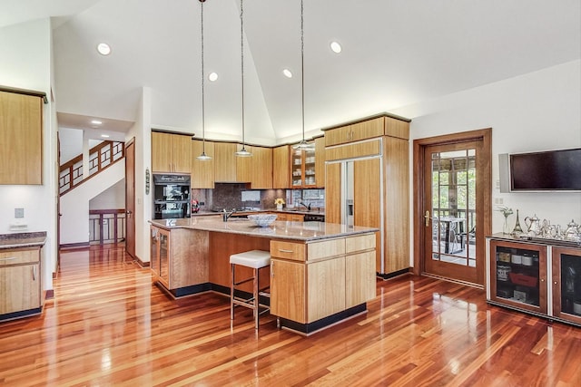 kitchen with a breakfast bar, high vaulted ceiling, an island with sink, decorative light fixtures, and wood-type flooring