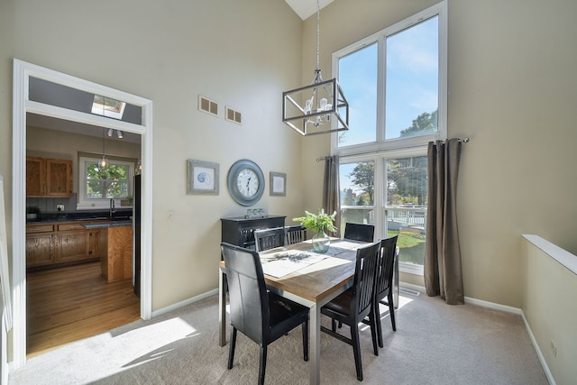 carpeted dining room with sink, a high ceiling, and a chandelier