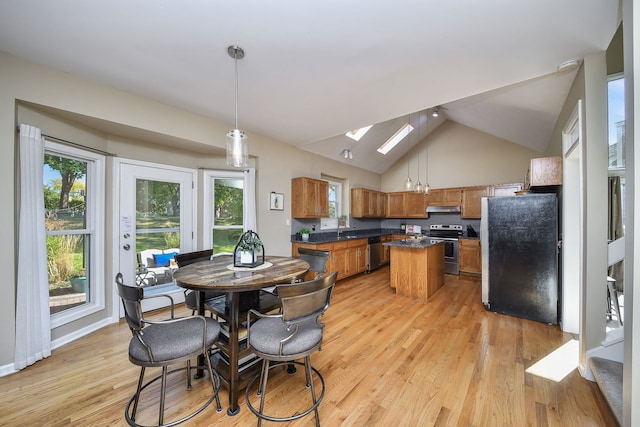 kitchen with hanging light fixtures, appliances with stainless steel finishes, light wood-type flooring, lofted ceiling with skylight, and a center island