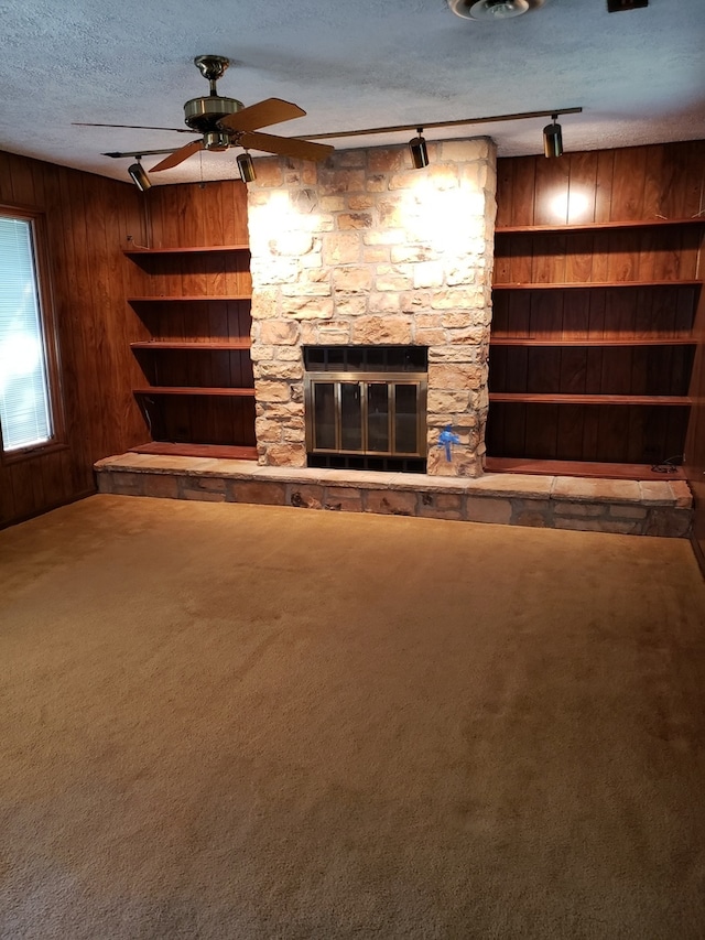 unfurnished living room featuring wooden walls, rail lighting, a fireplace, carpet floors, and a textured ceiling